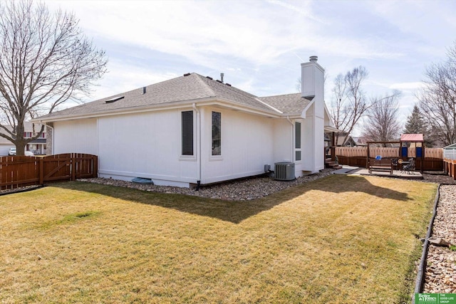rear view of property featuring a chimney, a fenced backyard, a shingled roof, and a lawn