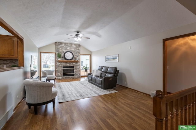 living room with a ceiling fan, vaulted ceiling, wood finished floors, and a fireplace