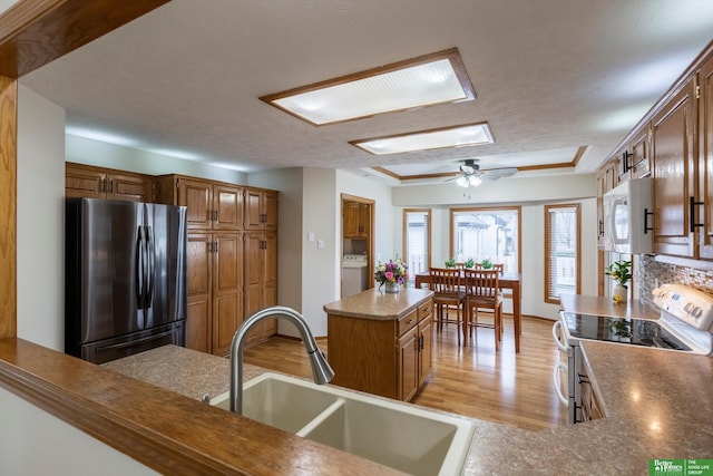 kitchen with a sink, range with electric cooktop, white microwave, washer / clothes dryer, and freestanding refrigerator