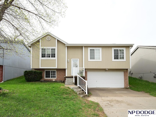 raised ranch featuring a front yard, driveway, an attached garage, and brick siding