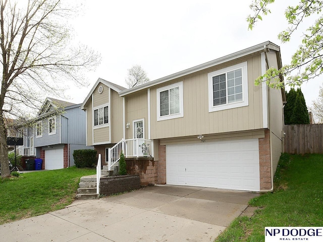 split foyer home featuring a front lawn, a garage, brick siding, concrete driveway, and fence