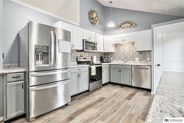 kitchen with hanging light fixtures, appliances with stainless steel finishes, a sink, light wood-style flooring, and tasteful backsplash