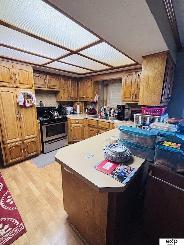 kitchen featuring light wood-style flooring, a peninsula, light countertops, a sink, and stainless steel range with electric stovetop