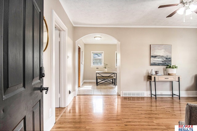 foyer with visible vents, baseboards, ceiling fan, light wood-type flooring, and arched walkways