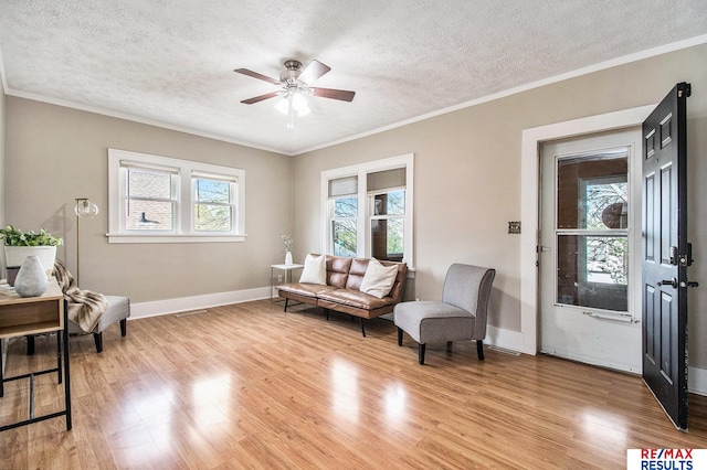 living area with baseboards, a ceiling fan, light wood-type flooring, and a textured ceiling