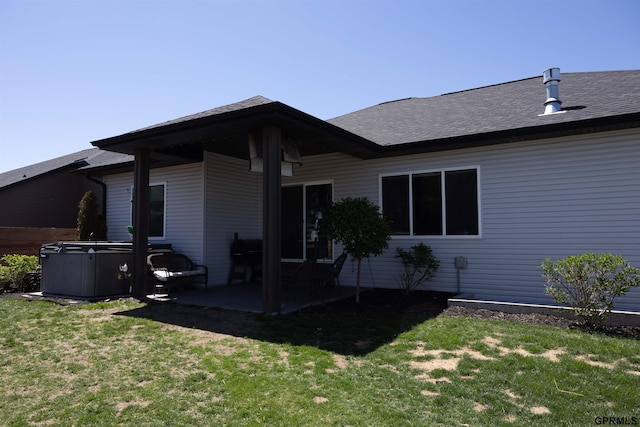back of house with a shingled roof, a patio area, a hot tub, and a lawn