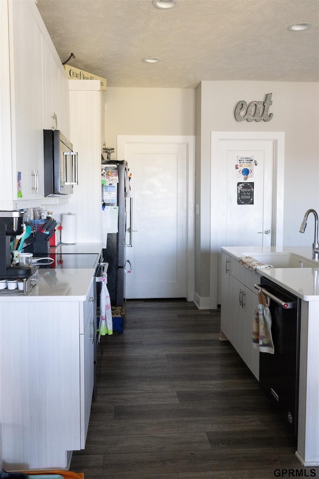 kitchen featuring stainless steel appliances, a textured ceiling, dark wood finished floors, a sink, and light countertops