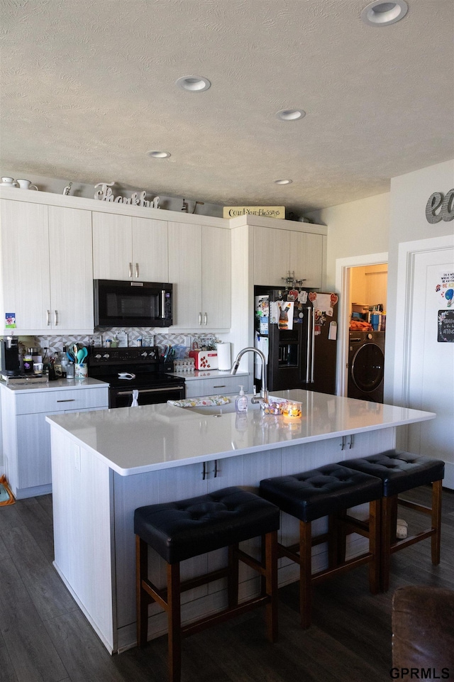 kitchen with light countertops, washer / clothes dryer, black appliances, and a breakfast bar