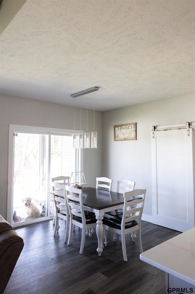 dining room featuring a textured ceiling, a barn door, and dark wood-style floors