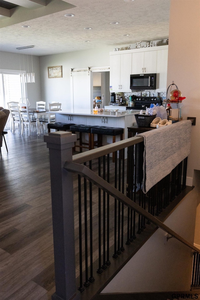 kitchen with dark wood-type flooring, recessed lighting, white cabinetry, black microwave, and backsplash