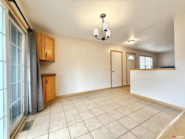 spare room featuring light tile patterned floors, visible vents, a chandelier, and baseboards