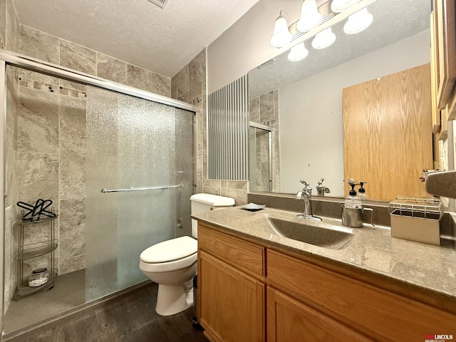 full bathroom with a textured ceiling, a shower stall, toilet, wood finished floors, and vanity