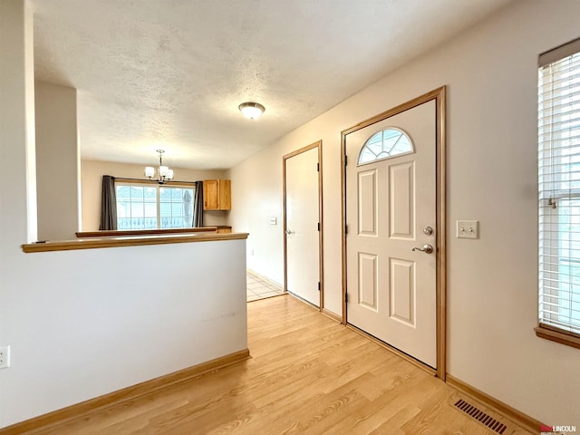 foyer featuring an inviting chandelier, visible vents, light wood-type flooring, and baseboards