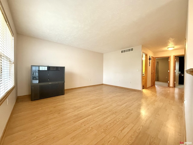 unfurnished living room featuring baseboards, visible vents, a textured ceiling, and light wood-style flooring