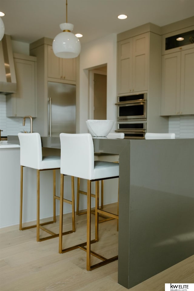 kitchen with decorative backsplash, light wood-style floors, stainless steel appliances, recessed lighting, and wall chimney exhaust hood