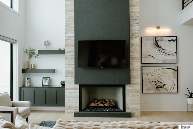 living area featuring baseboards, a high ceiling, wood finished floors, and a large fireplace
