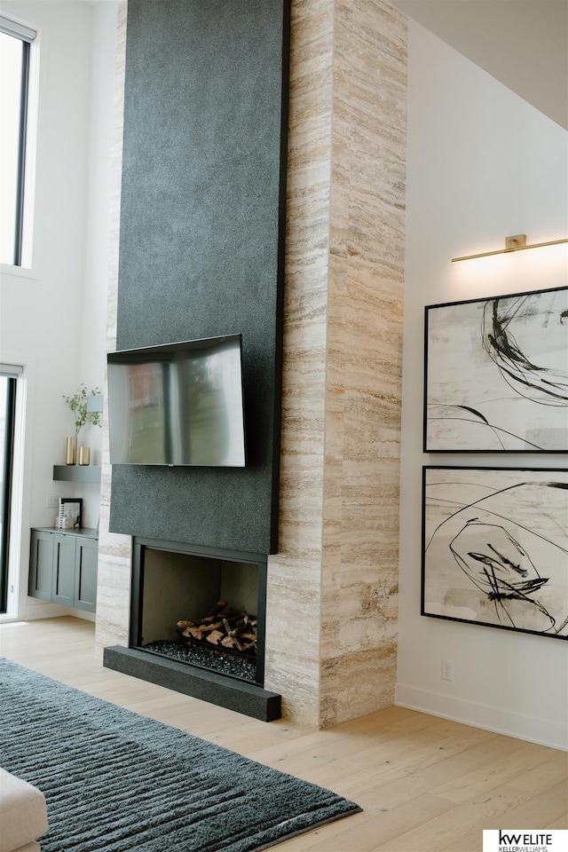 living area featuring a large fireplace, a high ceiling, baseboards, and wood finished floors