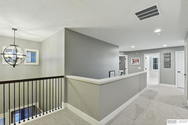 corridor with visible vents, an inviting chandelier, baseboards, carpet, and an upstairs landing