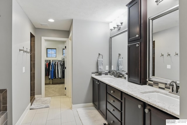 bathroom featuring double vanity, a sink, a walk in closet, and tile patterned flooring