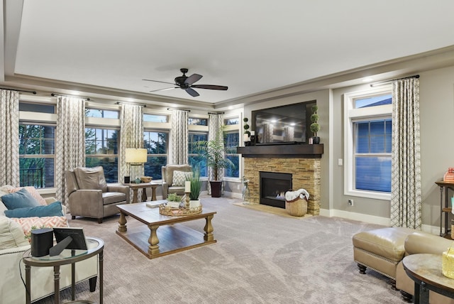 living area featuring crown molding, ceiling fan, carpet floors, a stone fireplace, and baseboards