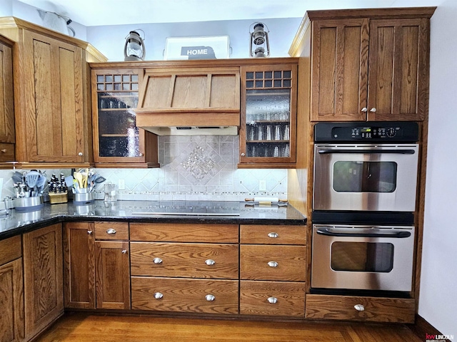kitchen featuring stovetop, double oven, wood finished floors, and tasteful backsplash