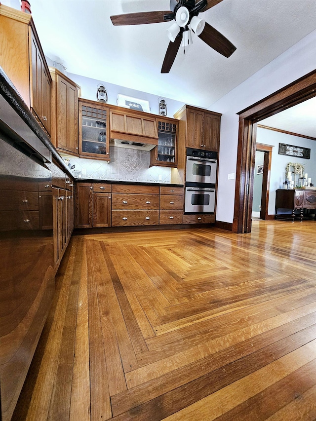 kitchen featuring tasteful backsplash, a ceiling fan, glass insert cabinets, and double oven