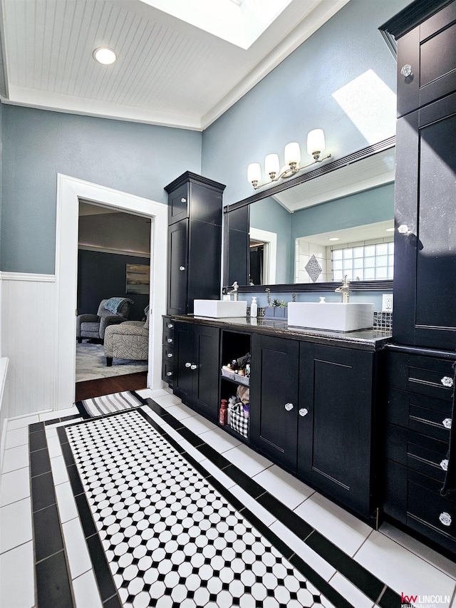 full bath featuring a skylight, connected bathroom, tile patterned floors, wainscoting, and vanity