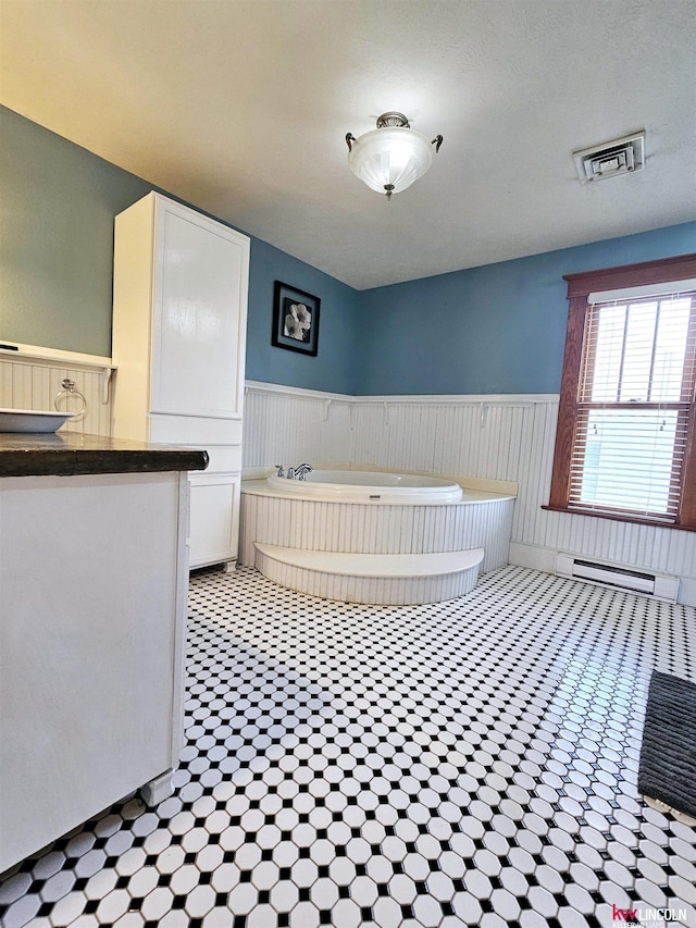 bathroom with a bath, a wainscoted wall, visible vents, and baseboard heating