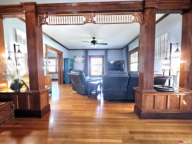 living area with crown molding, a ceiling fan, decorative columns, and wood finished floors