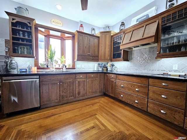 kitchen with tasteful backsplash, stainless steel dishwasher, glass insert cabinets, a sink, and dark countertops