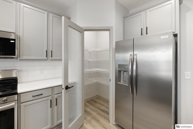 kitchen featuring tasteful backsplash, stainless steel appliances, light countertops, and light wood-style flooring