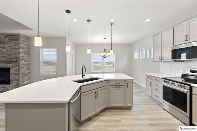 kitchen with a sink, stainless steel appliances, light wood-style floors, backsplash, and plenty of natural light