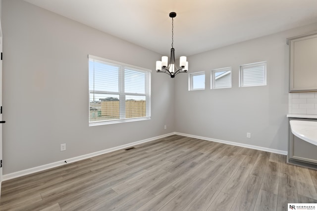 unfurnished room featuring an inviting chandelier, visible vents, light wood finished floors, and baseboards