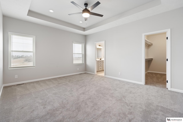 unfurnished bedroom with recessed lighting, a tray ceiling, a walk in closet, carpet, and baseboards