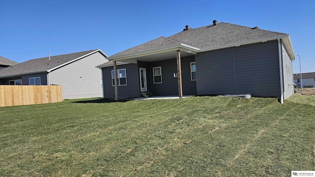rear view of property featuring a lawn, fence, a shingled roof, and a patio area