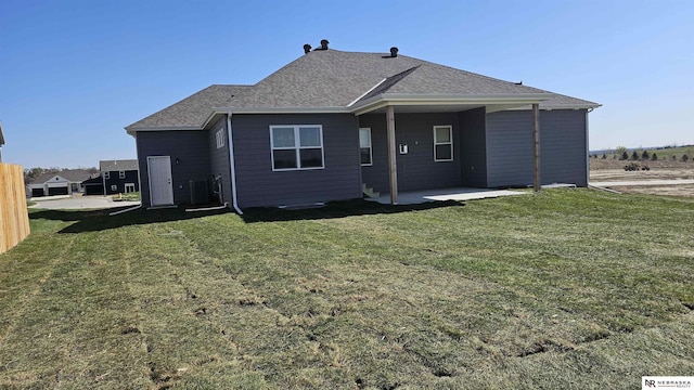 rear view of property with a lawn, a shingled roof, central AC unit, and a patio area