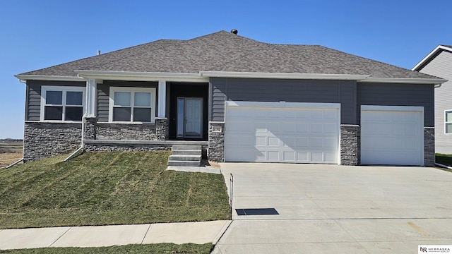 view of front of property with stone siding, roof with shingles, a front lawn, concrete driveway, and an attached garage