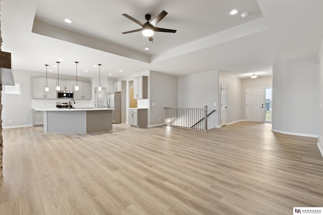 unfurnished living room with recessed lighting, a sink, ceiling fan, a tray ceiling, and light wood-style flooring