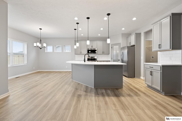 kitchen featuring a chandelier, stainless steel appliances, light countertops, backsplash, and gray cabinetry