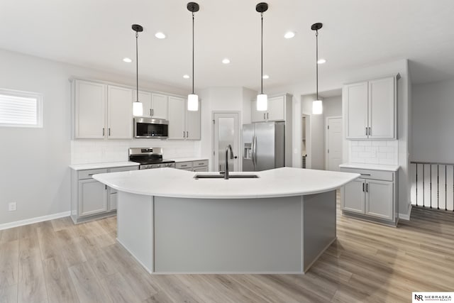kitchen featuring decorative backsplash, a sink, light wood-style floors, stainless steel appliances, and an island with sink