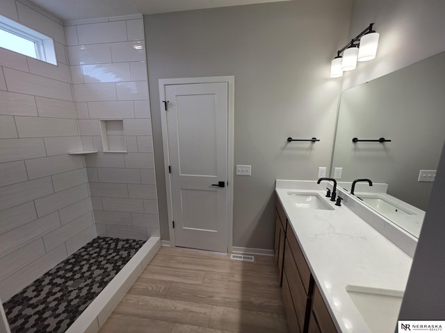 full bath featuring a tile shower, double vanity, a sink, and visible vents