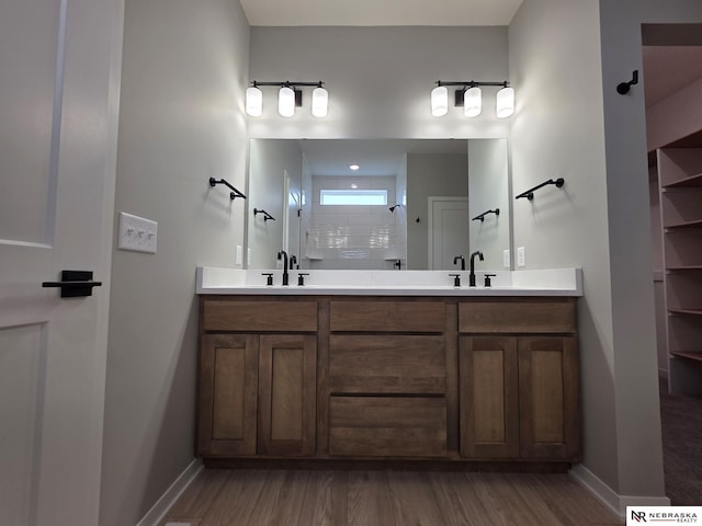 bathroom with wood finished floors, tiled shower, double vanity, and a sink