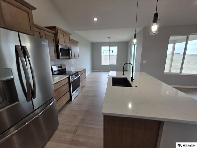kitchen with tasteful backsplash, a kitchen island with sink, appliances with stainless steel finishes, light wood finished floors, and a sink