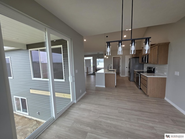 kitchen with pendant lighting, a sink, stainless steel appliances, light countertops, and baseboards