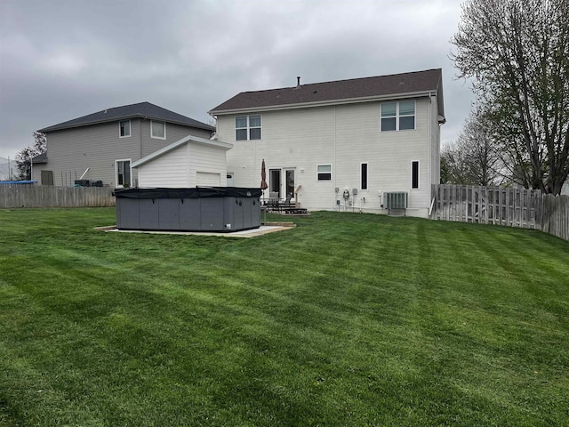 back of property with a yard, a hot tub, a fenced backyard, and central AC unit