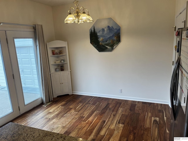 unfurnished dining area featuring dark wood-type flooring, a chandelier, and baseboards