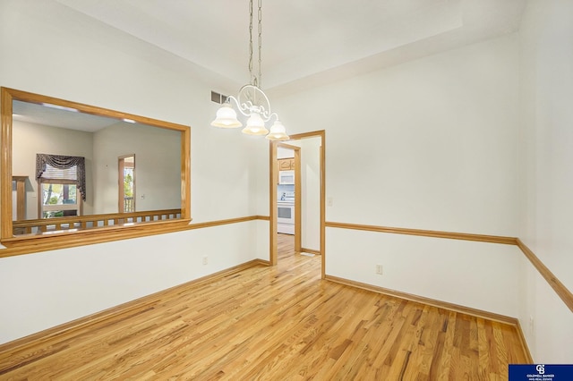 spare room with baseboards, a notable chandelier, wood finished floors, and visible vents
