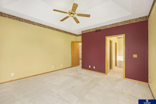 empty room with light colored carpet, a raised ceiling, a ceiling fan, baseboards, and visible vents