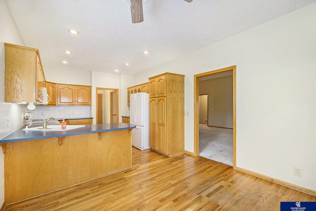 kitchen with a sink, light wood finished floors, white appliances, a peninsula, and a kitchen bar