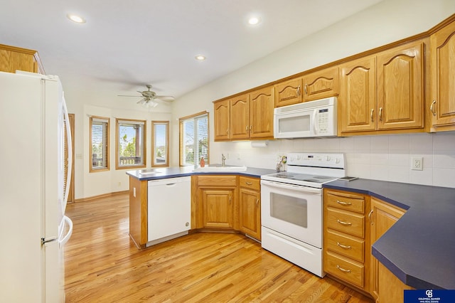 kitchen with a sink, light wood finished floors, a peninsula, and white appliances